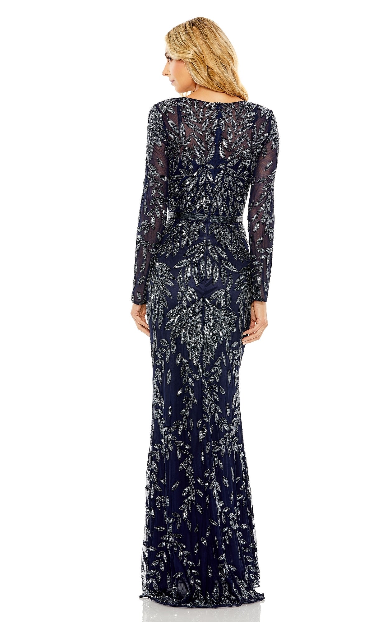 A woman stands facing away, wearing the Mac Duggal 6023 long blue beaded formal dress with silver leaf-patterned embellishments.
